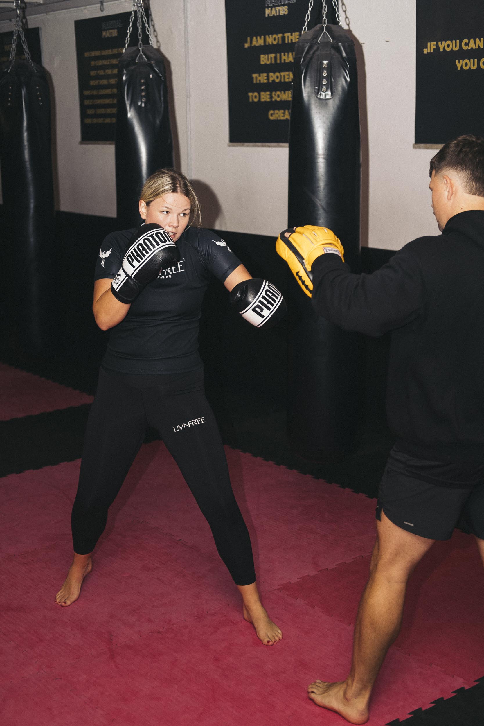 Kampfsportlerin im LivnFree Rashguard trainiert Boxtechniken mit einem Trainer im Kampfsportstudio. Fokus auf Schlagtechnik und Trainingseinsatz mit Handpratzen