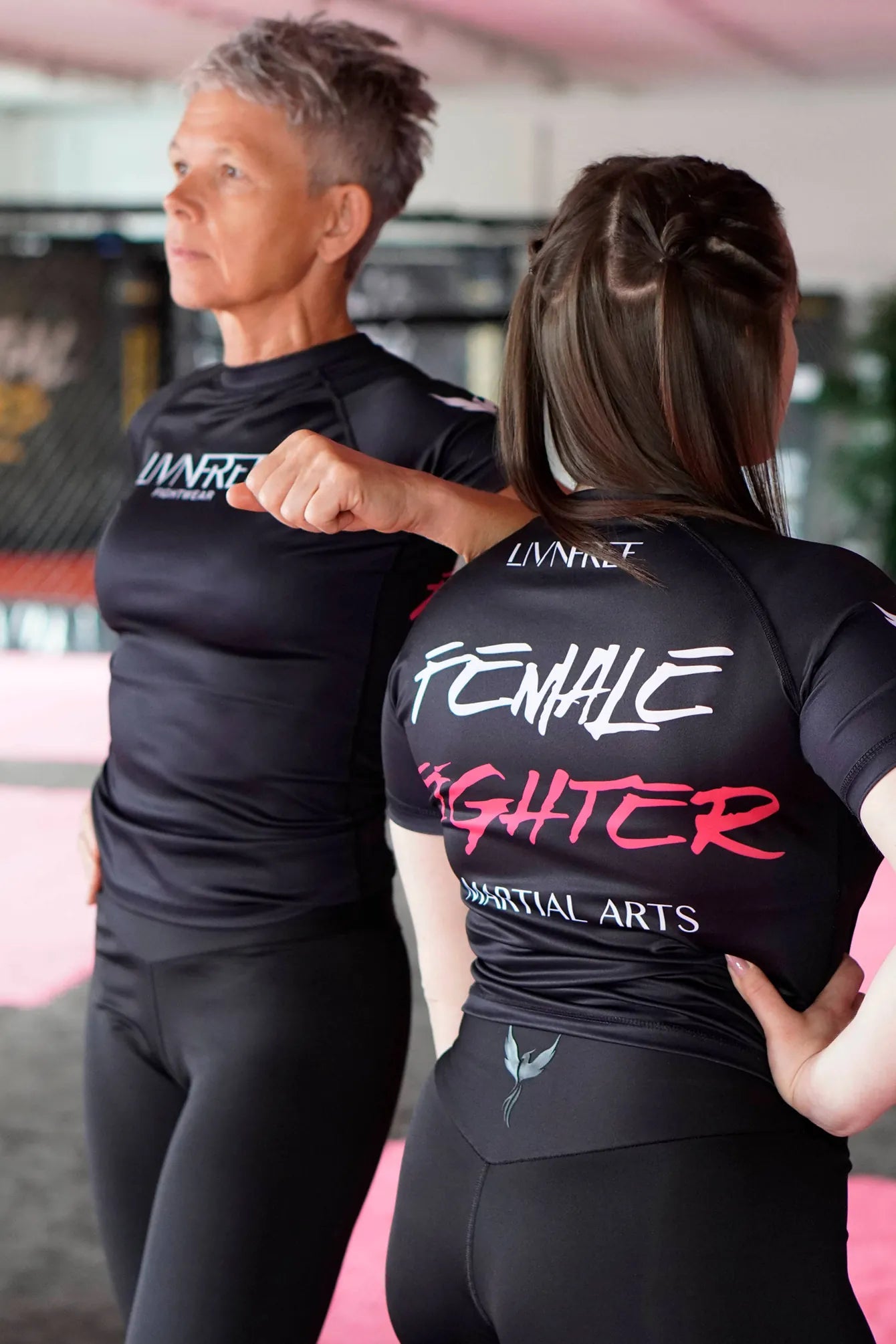 Zwei Frauen in Livnfree Fightwear Rashguards mit Aufdruck Female Fighter und schwarzen Sportleggings – Kampfsportkleidung für Frauen, die Stärke und Zusammenhalt verkörpert.