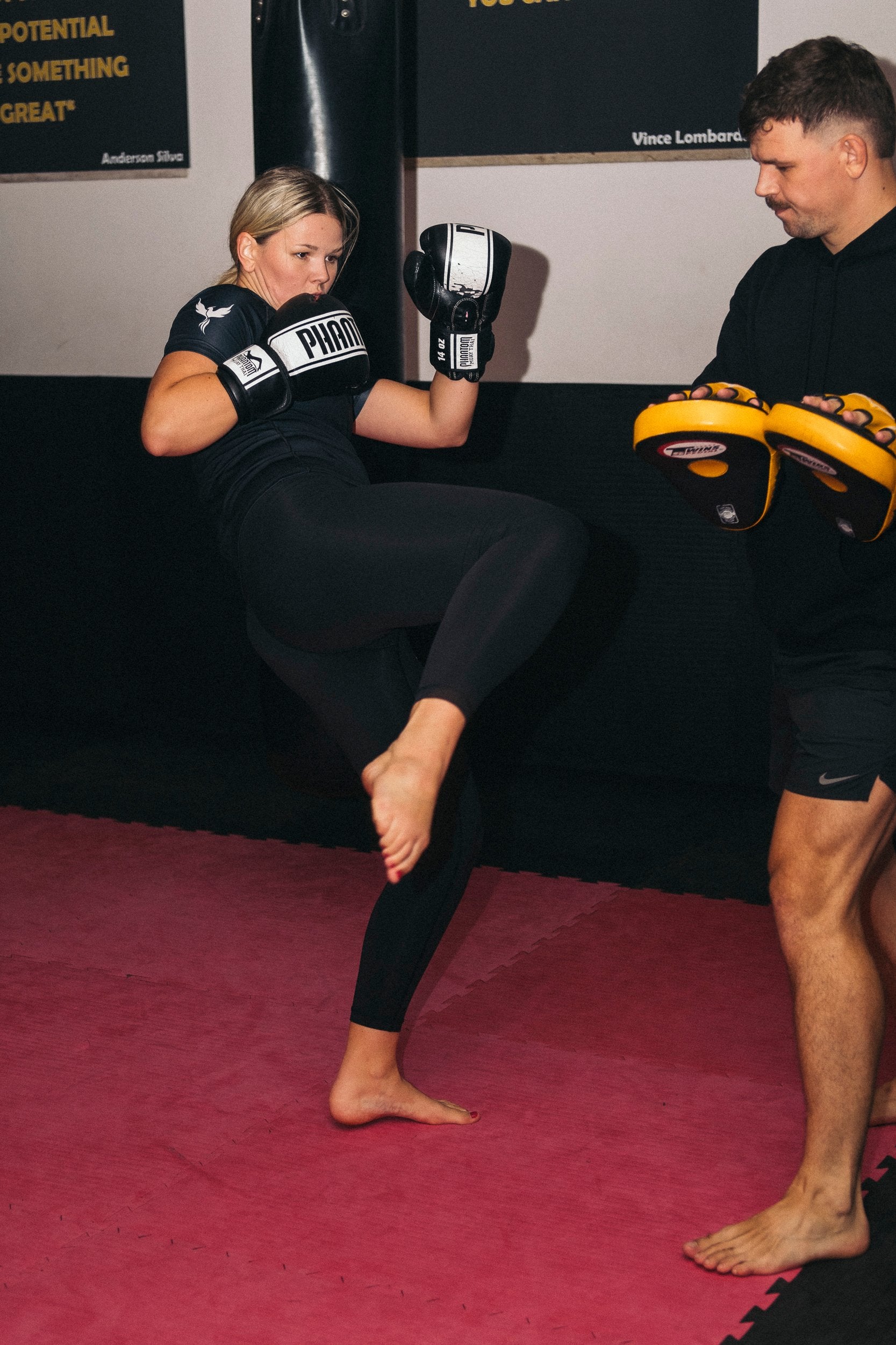 Frau im Kampfsporttraining, führt einen Kick mit Boxhandschuhen aus, während ein Trainer die Schlagpolster hält