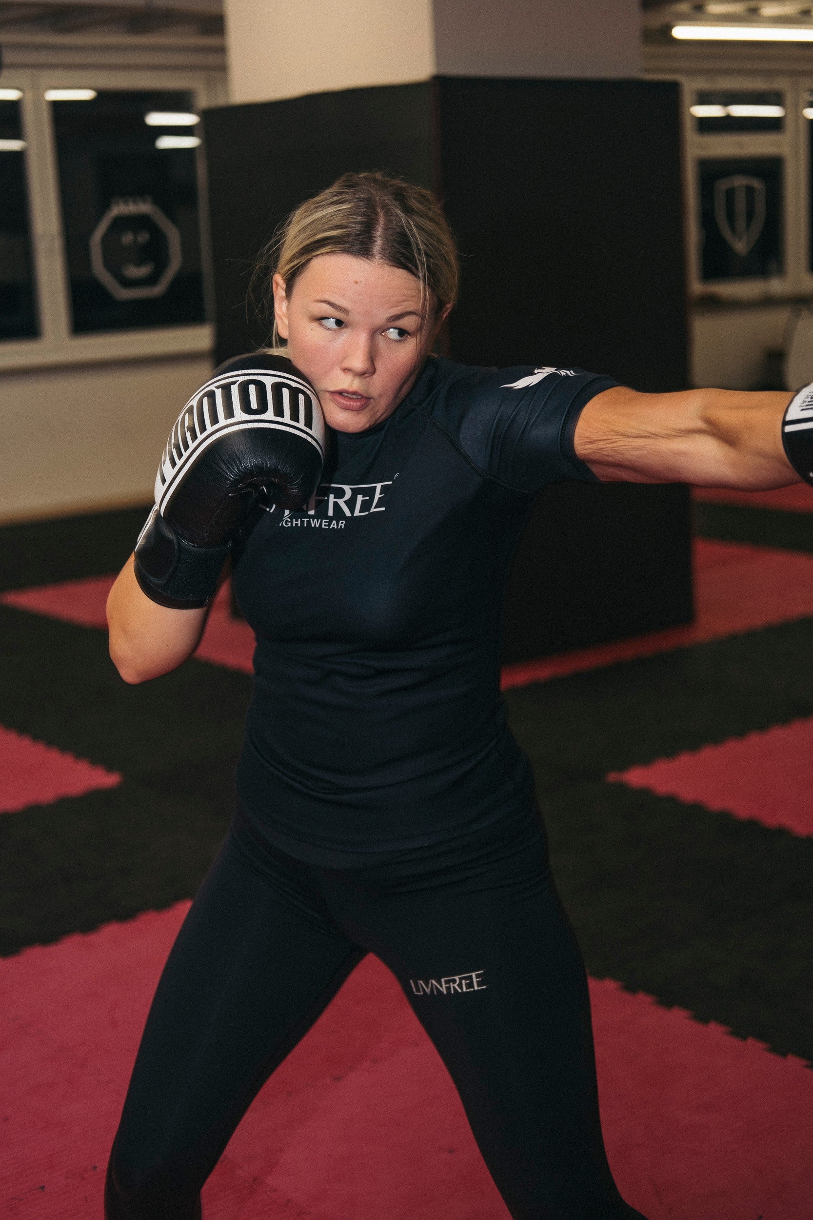 Frau im Kampfsportstudio in einer LIVNFREE Rash Guard führt einen Boxstoß aus, mit Boxhandschuhen und Fokussierung auf die Technik