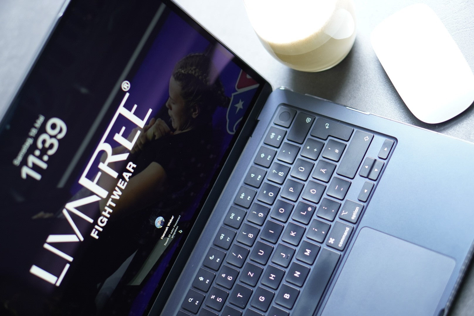 Laptop mit LivnFree Fightwear Hintergrundbild, begleitet von einer Tasse Kaffee und Maus – Darstellung von Kampfsportmarke für digitale Präsenz